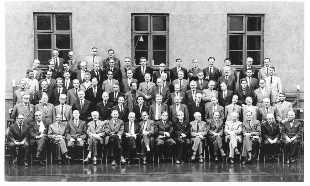 Dirac, seated in the front row between Aage Bohr and Otto Frisch, at the 1963 Niels Bohr commemoration conference in Copenhagen. Heisenberg is no. 4 from the right, and Jordan stands at the left in the second row. Credit: Niels Bohr Archive, Copenhagen.
