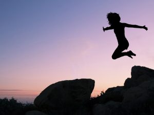 A silhouette of a person jumping off a mountain