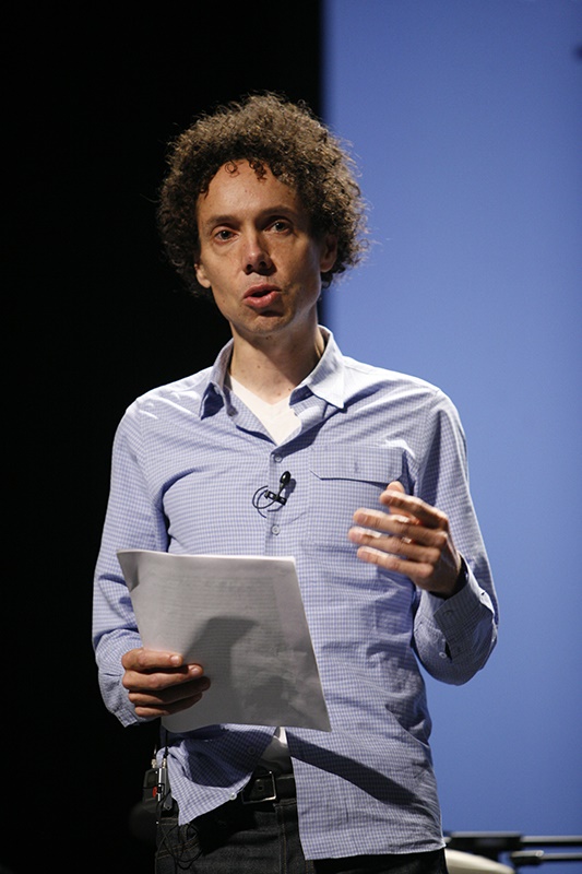A photo of Malcolm Gladwell holding a paper and wearing a microphone.