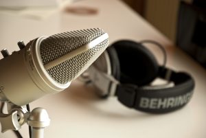 A silver podcasting microphone and a black headset sit on a white table.