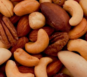 A variety of nuts are piled up, The center nut is a large cashew.