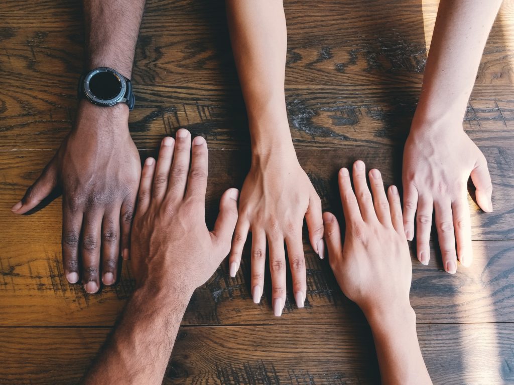 Five people place their hand on a a wooden table