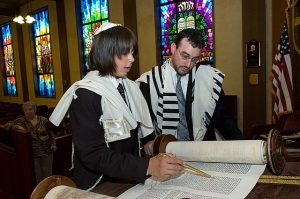 A photograph of a Jewish boy reading the Torah at his Bar Mitzvah, using a Yaad (A Torah pointer)