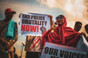 Protesters hold signs saying "End police brutality now."