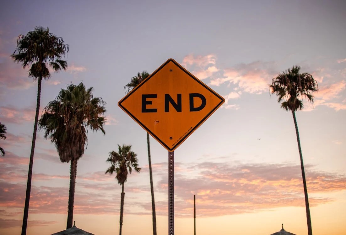 Street sign that says "END" and is in front of palm trees and a sunset or sunrise