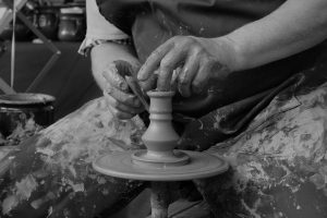 A seated figure throws a pot on a wheel.