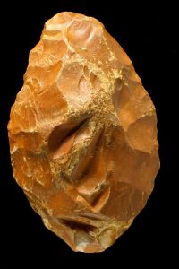 A brown chipped stone tool against a black background.