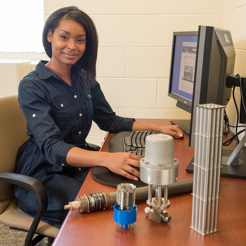 photo of woman sitting at computer desk with machine parts on the desk