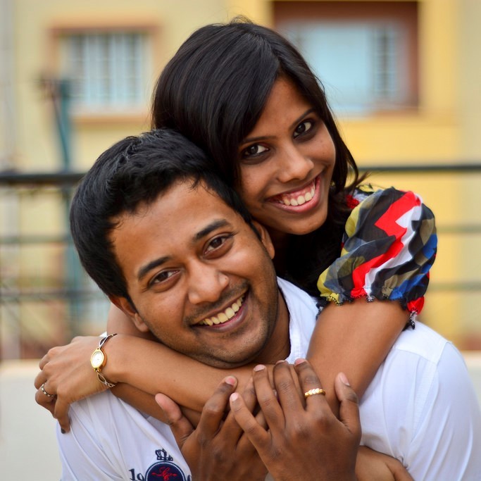 A photo of a woman hugging a man from behind. Both people are smiling