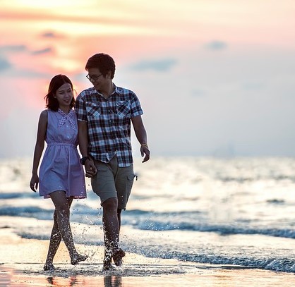 photo of two people holding hands walking on the beach at sunset