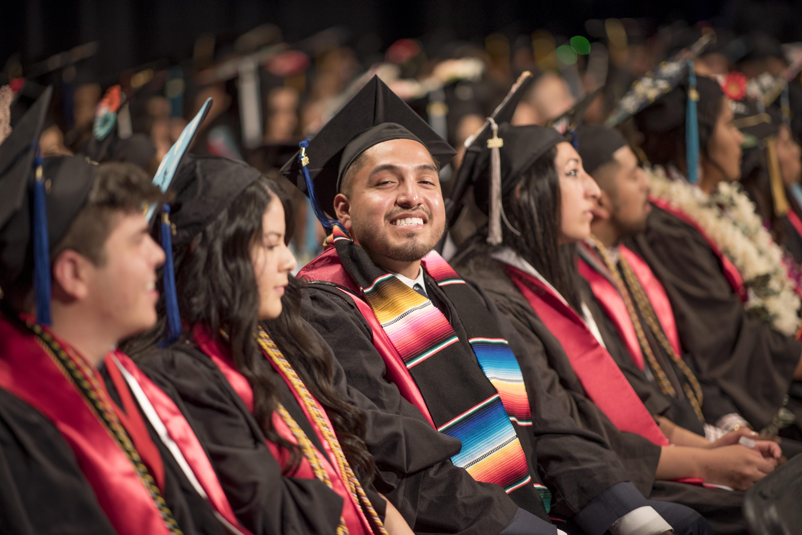 A line of college graduates sitting in an auditorium at graduation, with their caps and gowns. Christopher Marin (center) and fellow students are celebrated during the Latinx graduation celebration in the Laxson Auditorium on Saturday, May 19, 2018 in Chico, Calif.