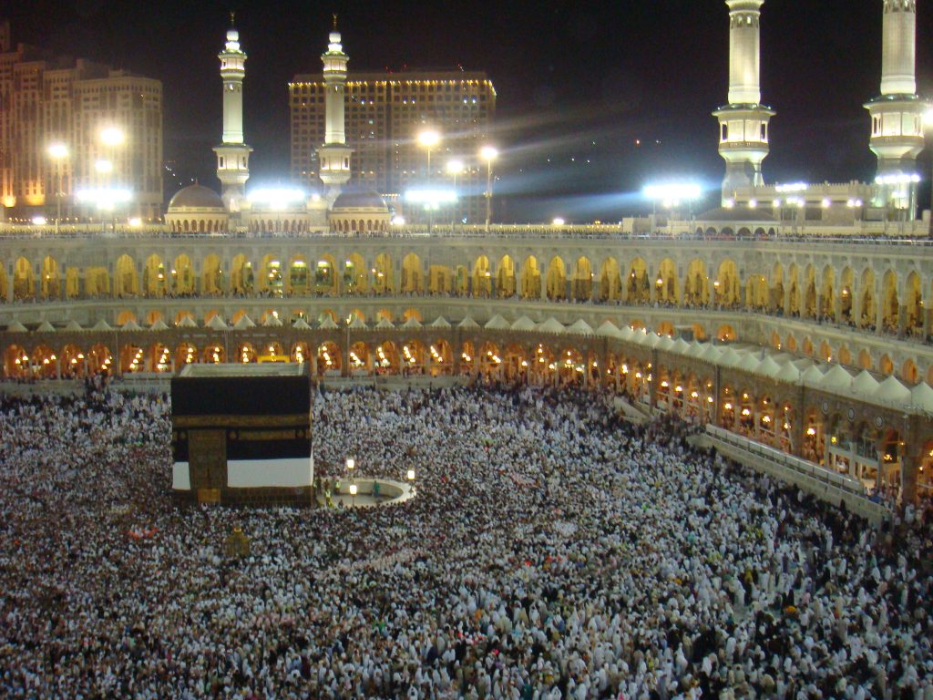 The Kaaba in the center of the the Masjid al-Haram in Mecca, Saudi Arabia. It is a large cube, draped in black cloth and is surrounded by worshippers