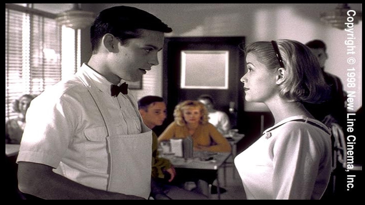 Black and white film still of a man and woman in a diner, facing each other. In the background, two other characters who have been colourized sit at a table.