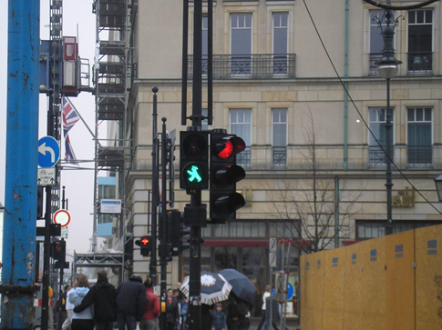 This image of an urban scene includes traffic lights in the center. The light on the left has a green walk signal, and on the right the red stop light is lit.