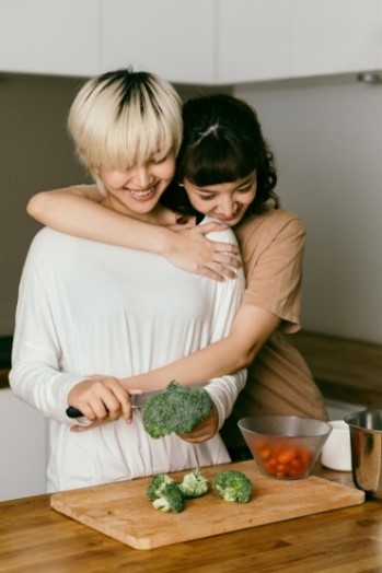 Man chopping vegetables while woman hugs him from behind