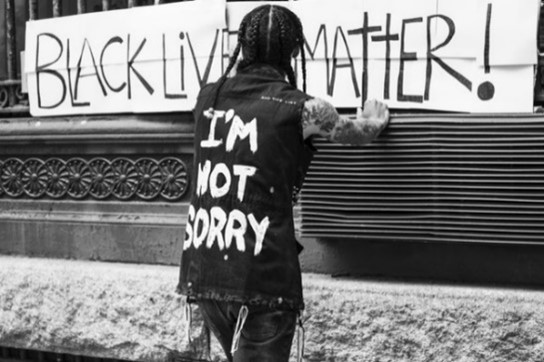 Man wearing vest that says, "I'm not sorry" standing in front of a Black Lives Matter banner
