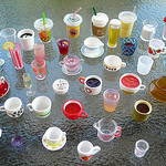 A wide range of types of teas in fancy tea cups, mugs, and take-away glasses are displayed in this image.