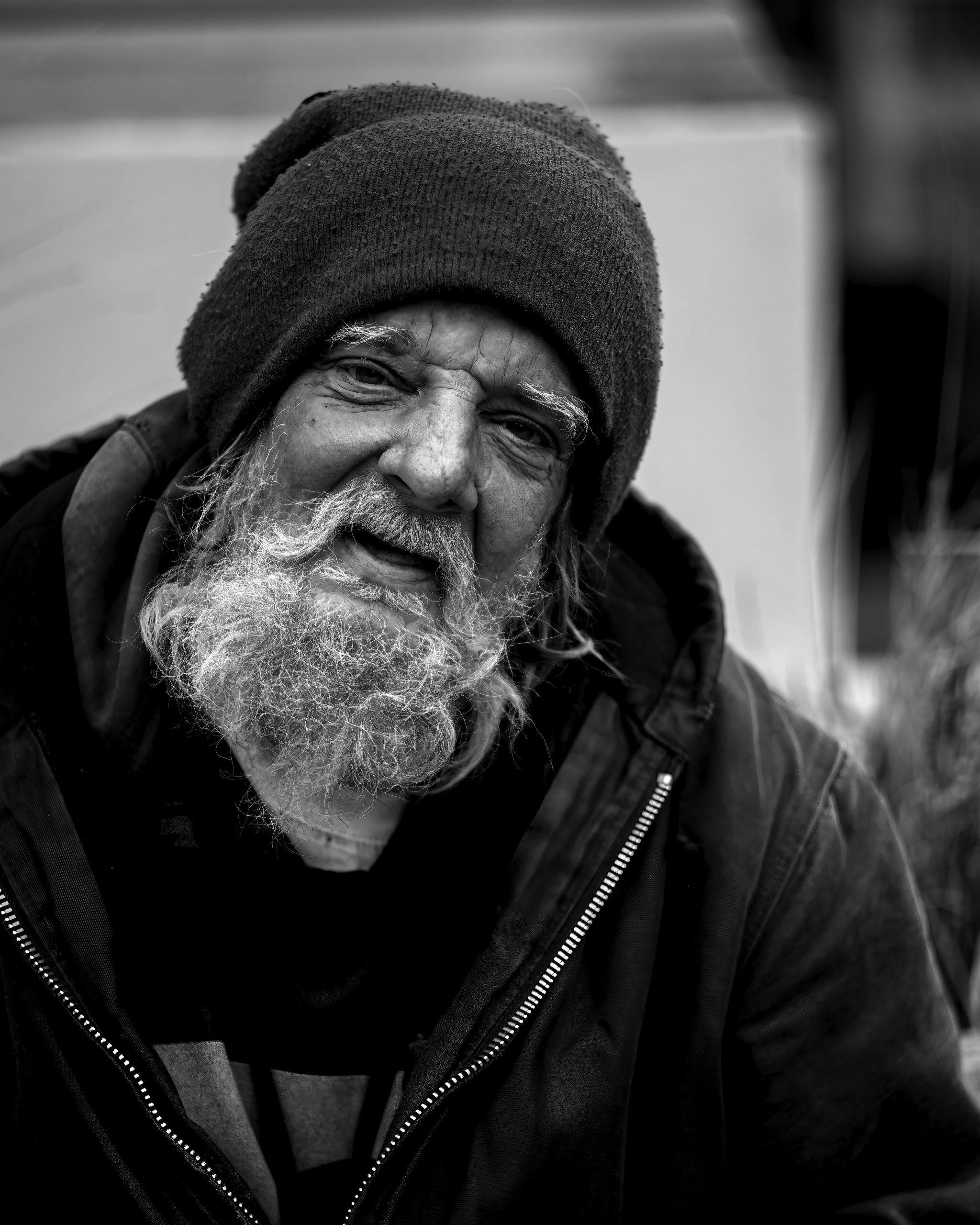 Image shows an old man with a hat, jacket, and beard. The image is in black and white