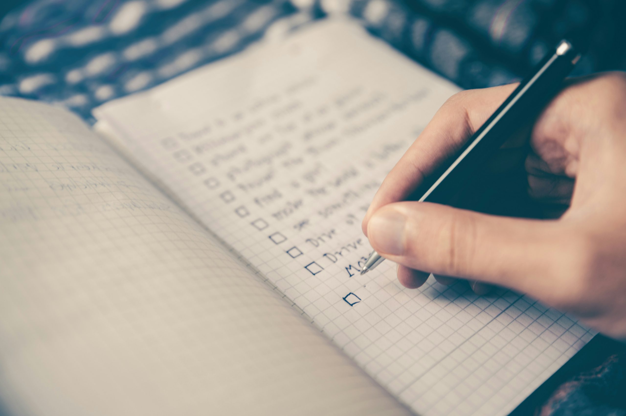 Photo of a notebook with a hand holding a pen and making a list
