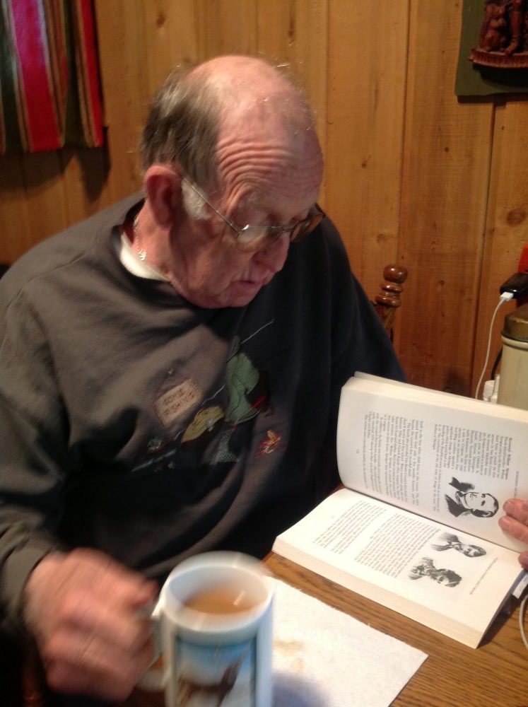 Picture for decorative purposes. Elderly man reading a book and drinking a cup of coffee.