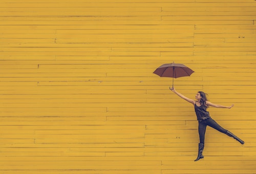 Person with opened umbrella leaping in front of a yellow wall