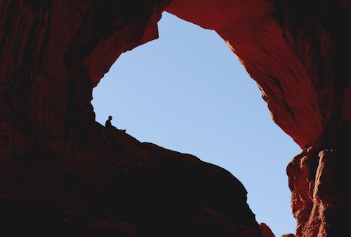 Hiker perched on ledge of canyon cave opening