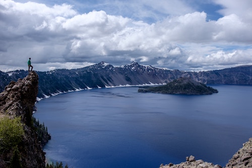 Hiker on ledge looking down into Crater Lake
