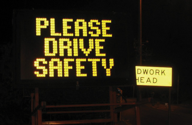 A lit up road sign saying "Please drive safety"