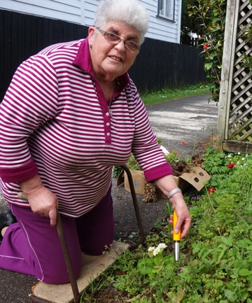 Lesley kneeling beside a small area of garden with bright orange trowel and fork