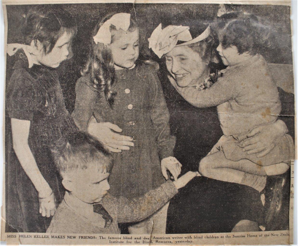 Helen Keller seated and smiling, with four children from the Blind Institute. Lesley is kneeling on Helen's lap with arm around her neck.