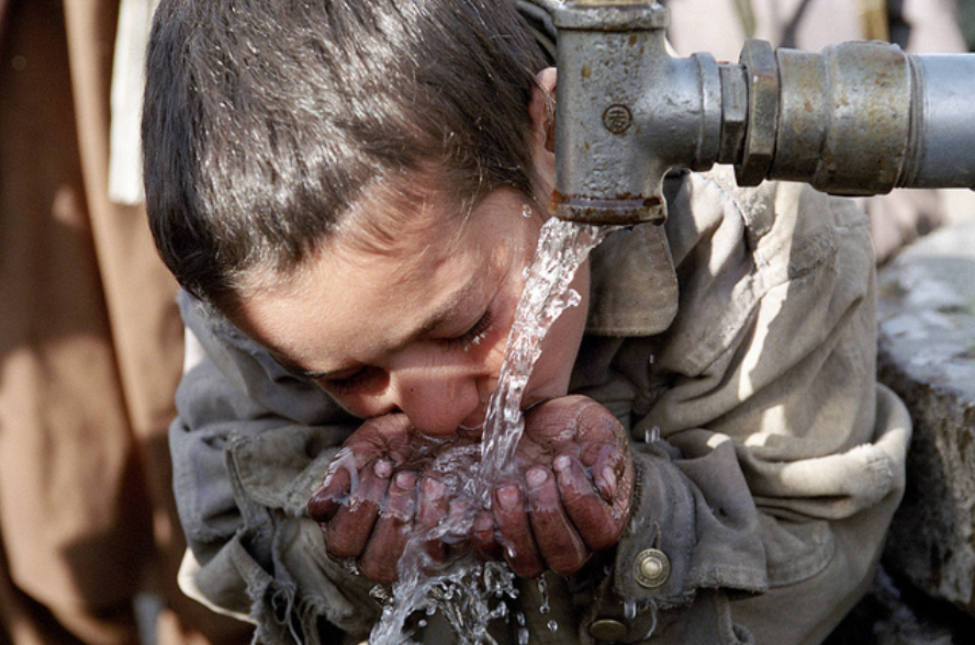 child drinking water with hands from a pipe