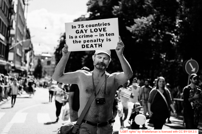 Picture of man with a sign saying in 75 countries gay love is a crime - in ten the penalty is death