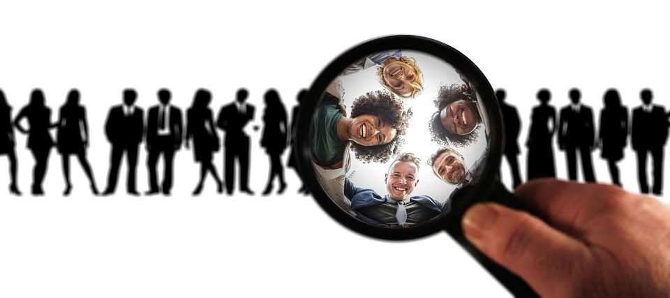 a row of people in silhouette with five people illuminated by a magnifying glass