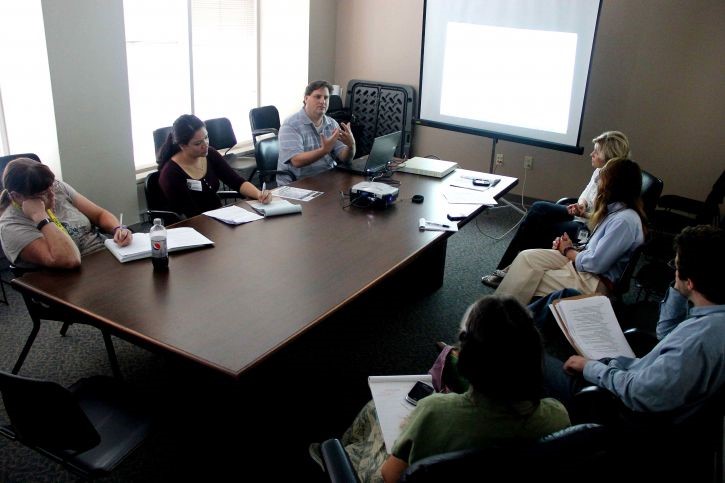 seven people sitting around a table talking and taking notes