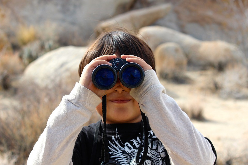 young boy peering through binoculars in a desert
