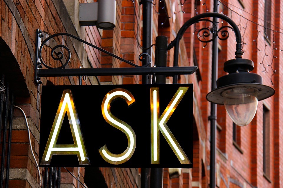 an illuminated street sign that reads "ask"