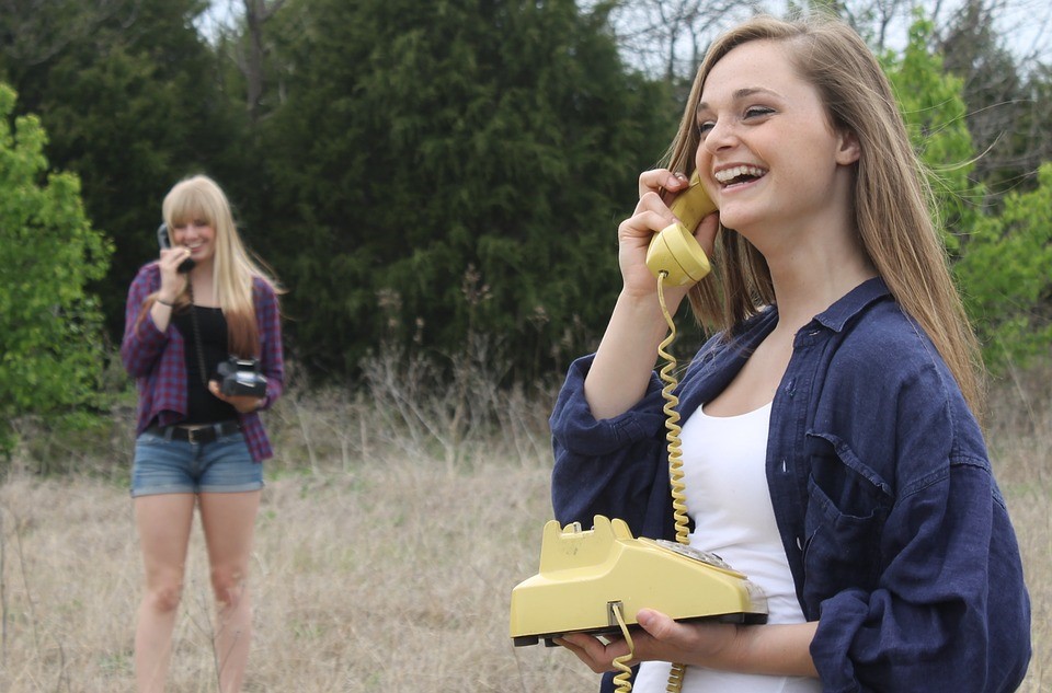 two girls in a field holding phones and laughing