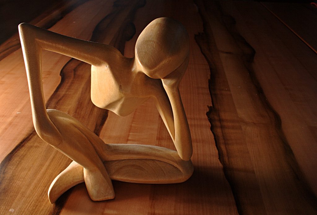 An abstract wooden sculpture of a human figure deep in thought