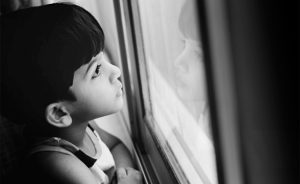 This photo depicts a young boy with dark hair looking out the window