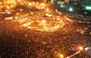Photo of a crowded Tahirir Square in Cairo, Egypt where many people in the crowd are waiving Egyptian flags in the air.