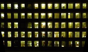 A photo of a large office building at night where you can see many people working inside after hours