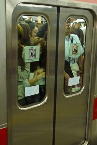 A crowd of people behind closed subway car doors is shown