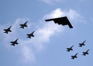 A formation of airplanes featuring fighter jets and a stealth bomber is shown in the sky