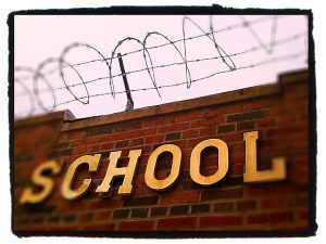 A brick wall is shown with the word "school" on it and barbed wire on top