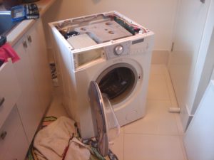 A broken washing machine is shown with no top cover