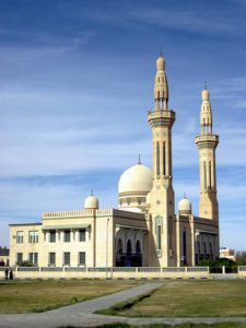 A mosque is shown, a large building with one large dome and two smaller domes and two towers, called minarets