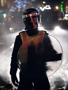 A masked officer with a shield is shown here