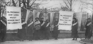 Figure (a) shows women's suffrage marchers