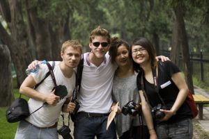 Four smiling friends holding cameras standing closely together while posing for a photograph.