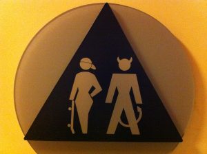 A coed bathroom sign depicting a skater woman and devil man.